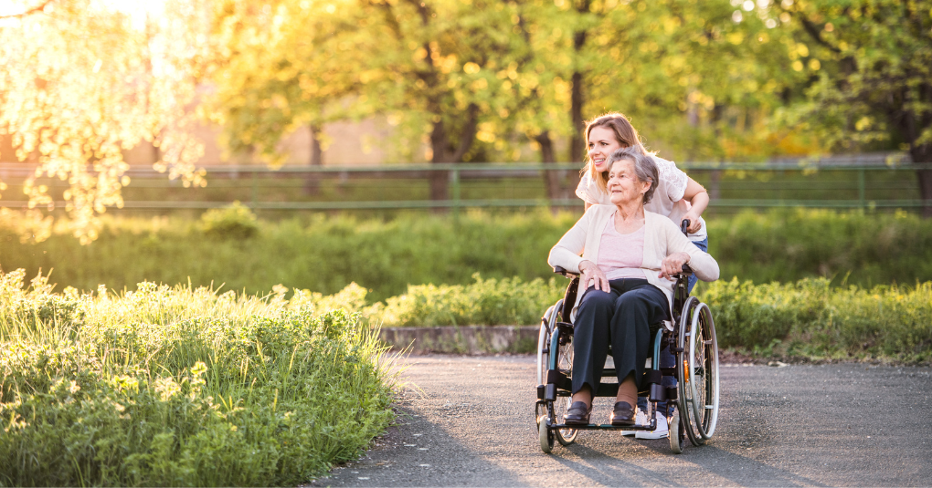 Female in wheelchair being pushed by another female in outdoor garden.