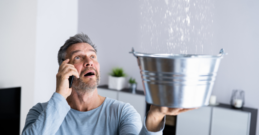 Male on phone holding bucket as rain falls into bucket.