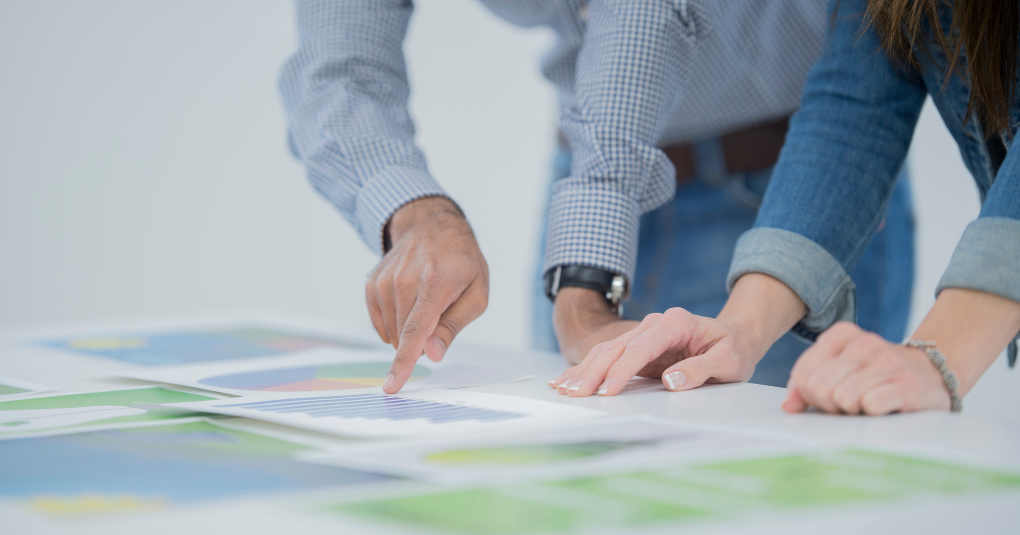 Two sets of hands pointing to paper planning documents on tabletop.